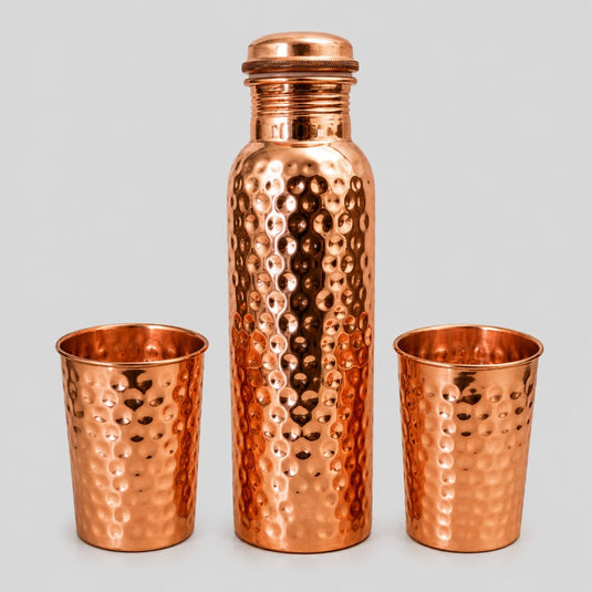 Copper hammered water bottle and two cups on a light gray background