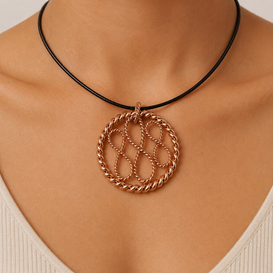 A close-up of a person's neck and chest wearing a black cord necklace with a circular rose gold pendant featuring an interlocking infinity symbol design.